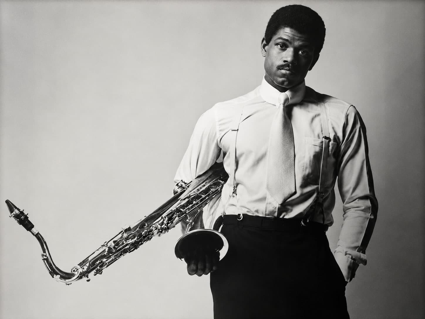 Man in Shirt and Suspenders Holds Saxophone in Studio Portrait